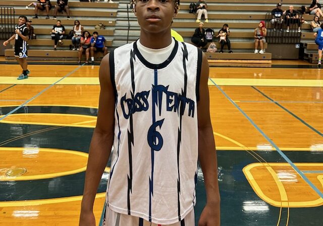 Young basketball player in a white and blue jersey standing on a gym court.