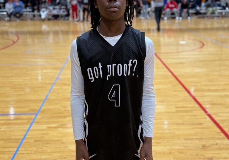 Young basketball player standing on court in uniform with "got proof?" text.