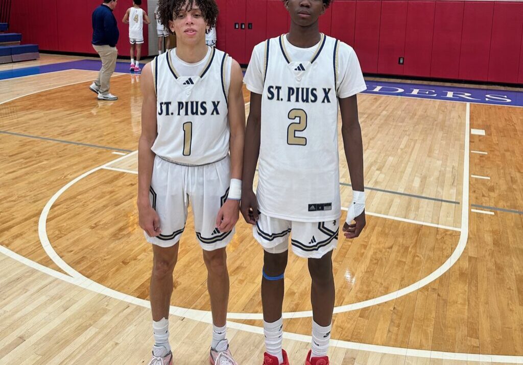 Two basketball players in matching St. Pius X uniforms standing on a court.