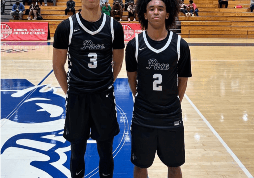 Two basketball players in black jerseys posing on court.