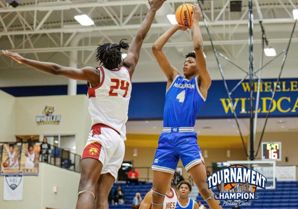 Basketball player in blue jumps to shoot while defender in white jumps to block.